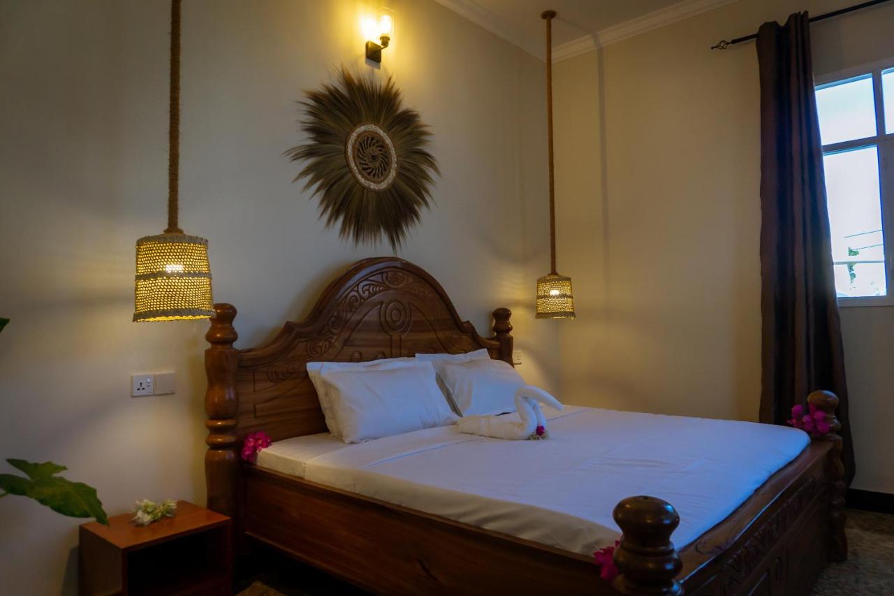 A king bed dressed in white linen beneath a carved headboard, warmly lit